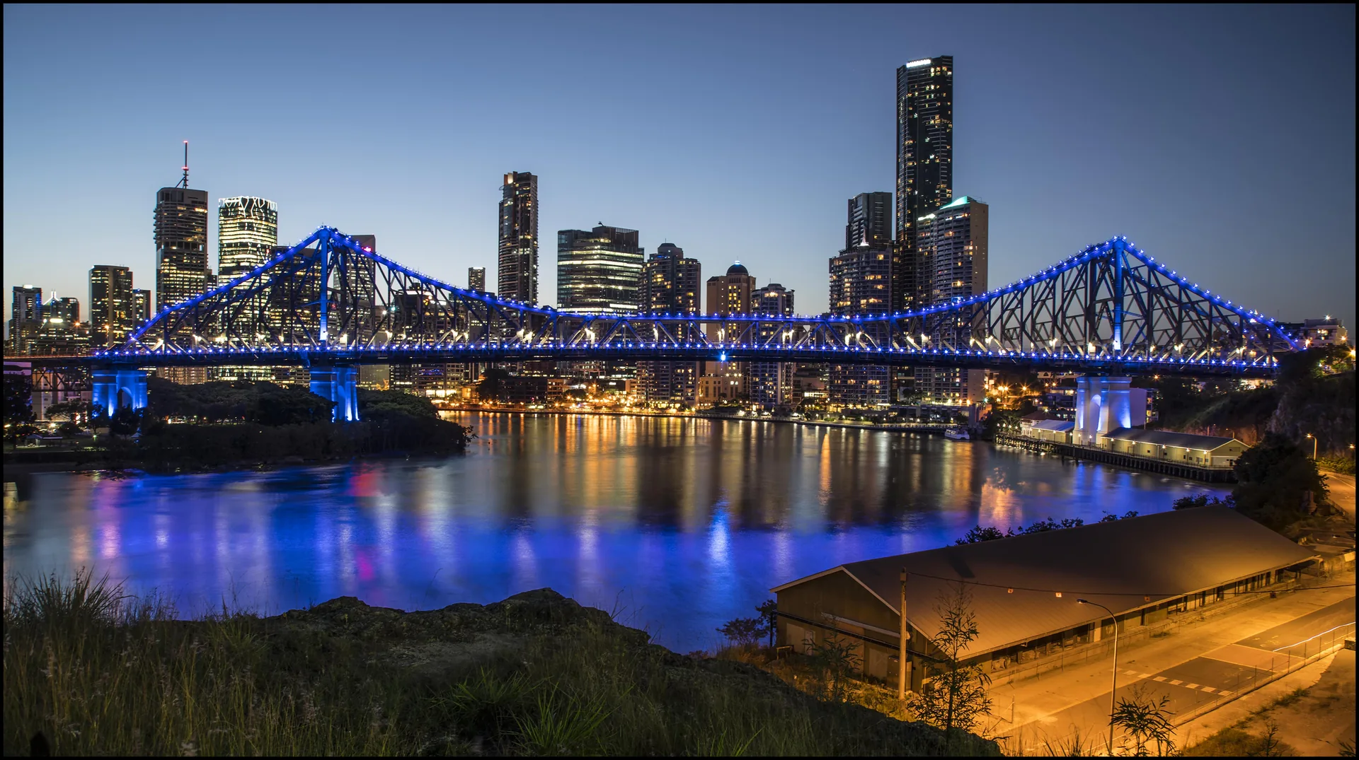 The illuminated Story Bridge spans the Brisbane River at dusk.