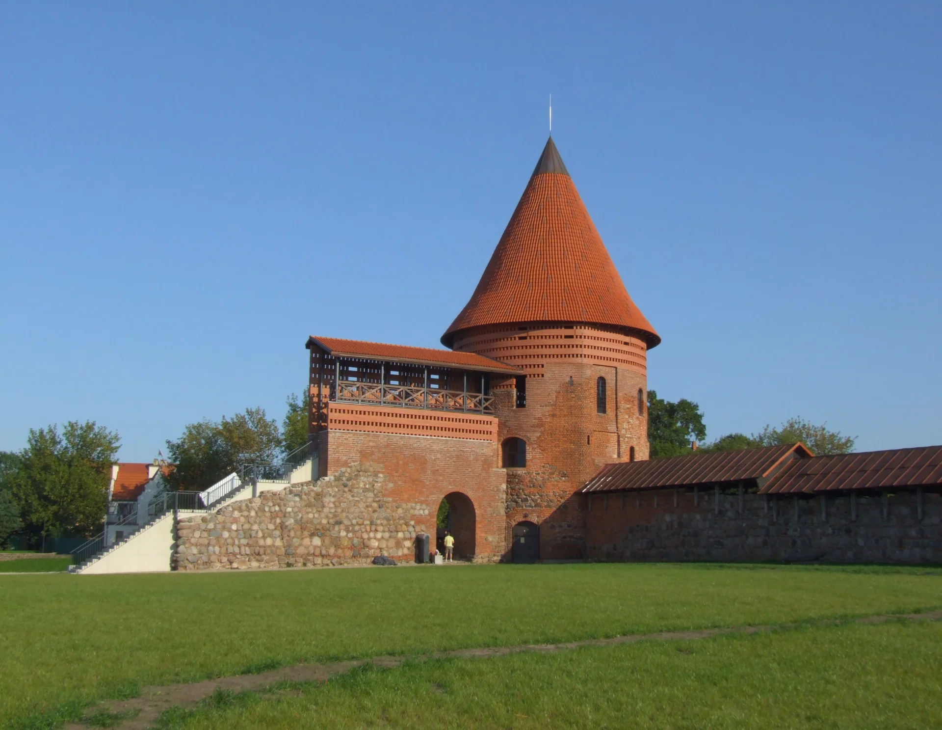 Red-roofed round tower and stone walls of Kaunas Castle above a green lawn
