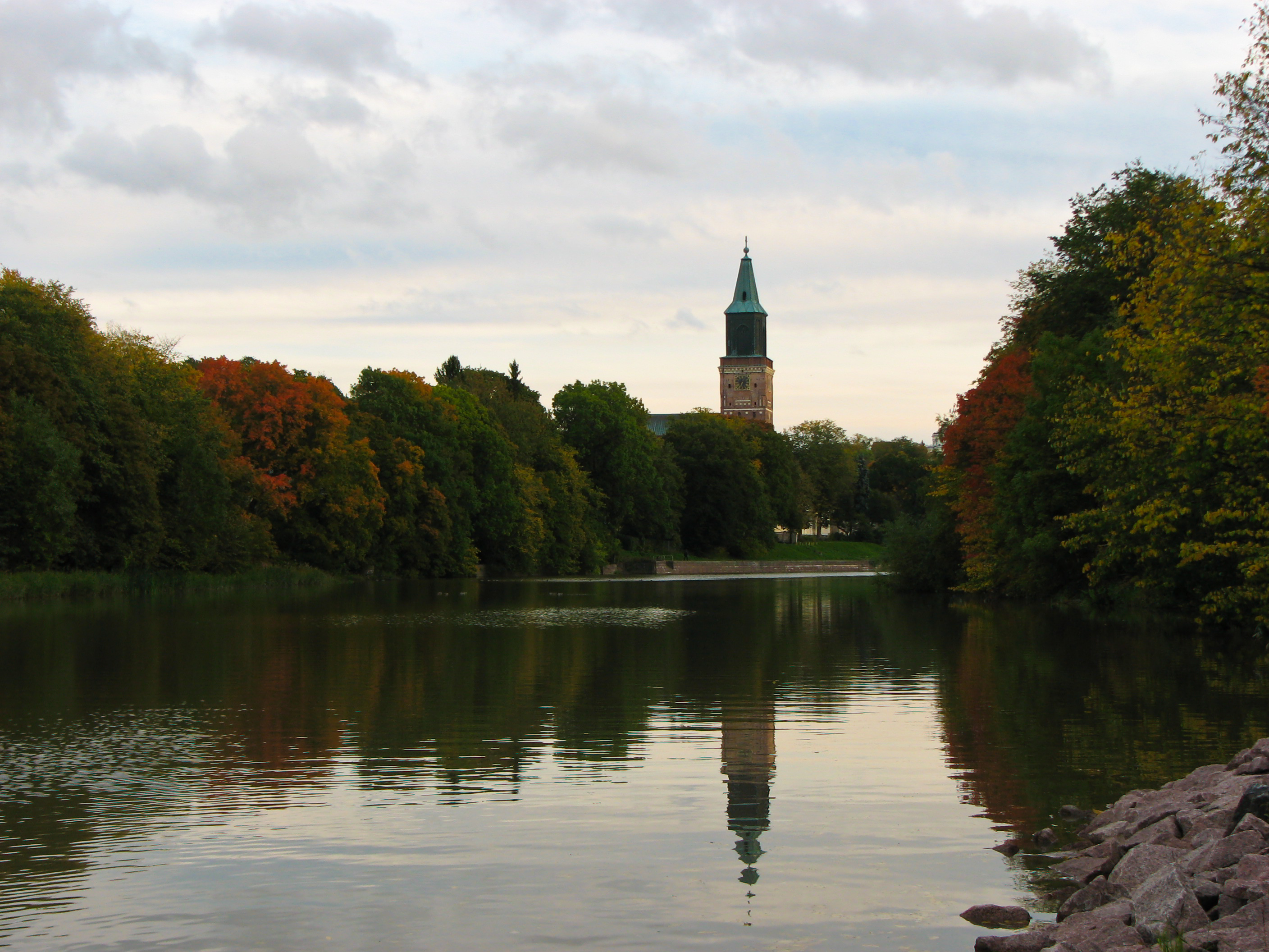 Turku Cathedral’s green spire reflected in the Aura River among autumn trees