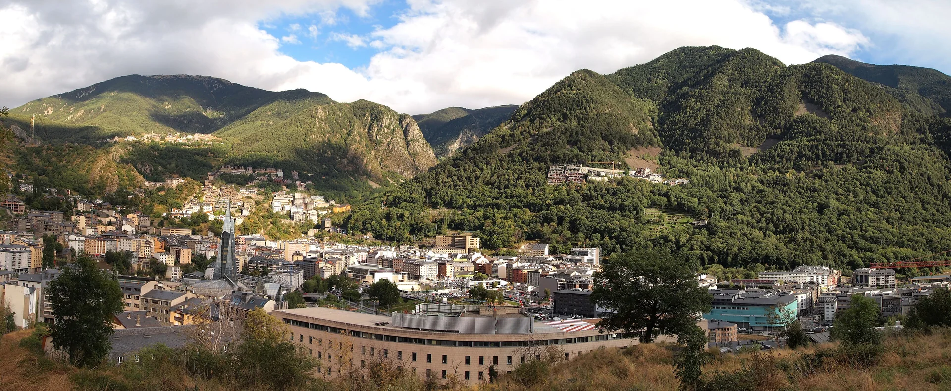 Caldea’s glass spire and surrounding buildings below forested mountains in the central Andorran valley
