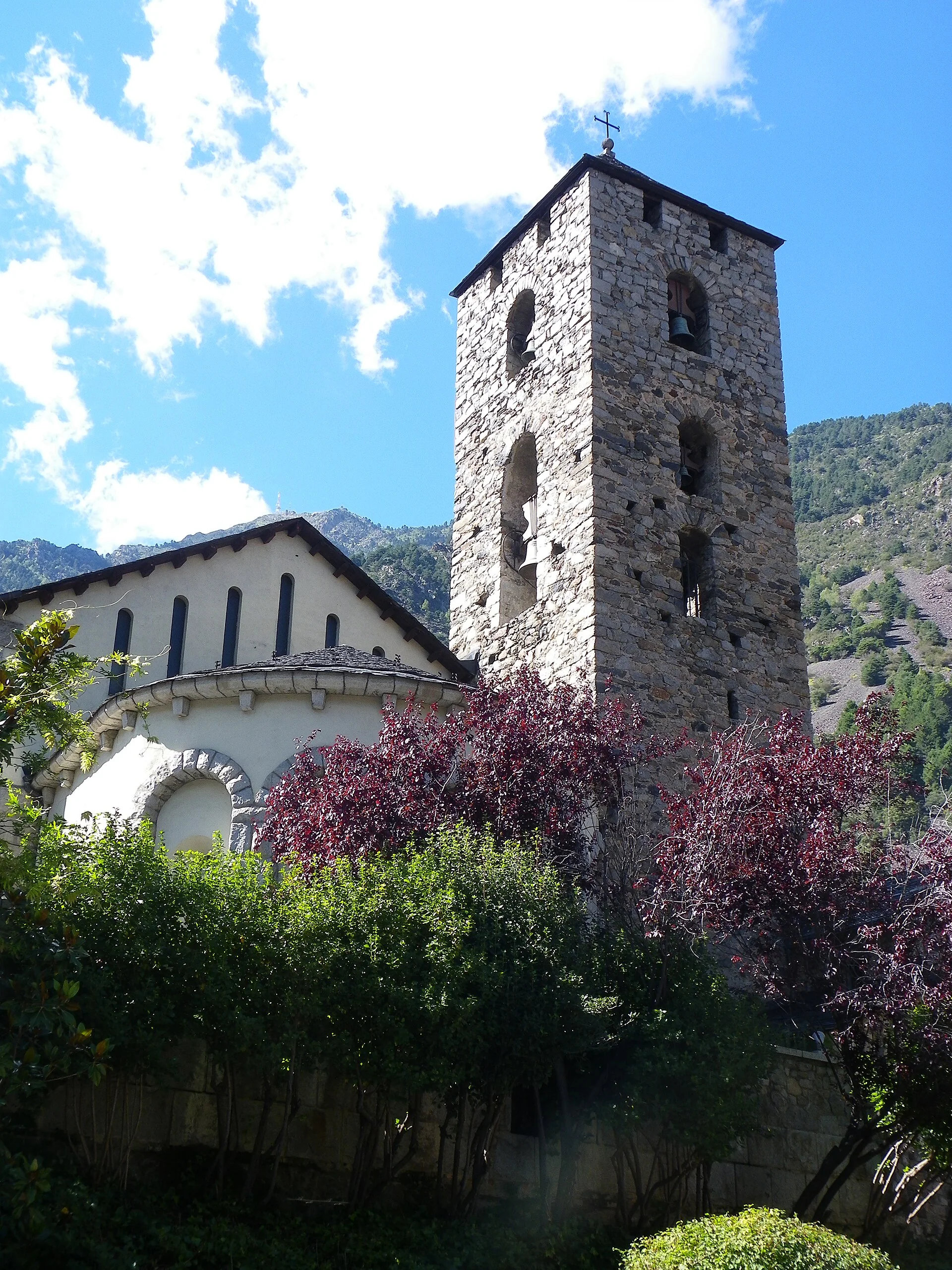 Sant Esteve’s stone bell tower and Romanesque apse framed by trees and the mountains of Andorra la Vella