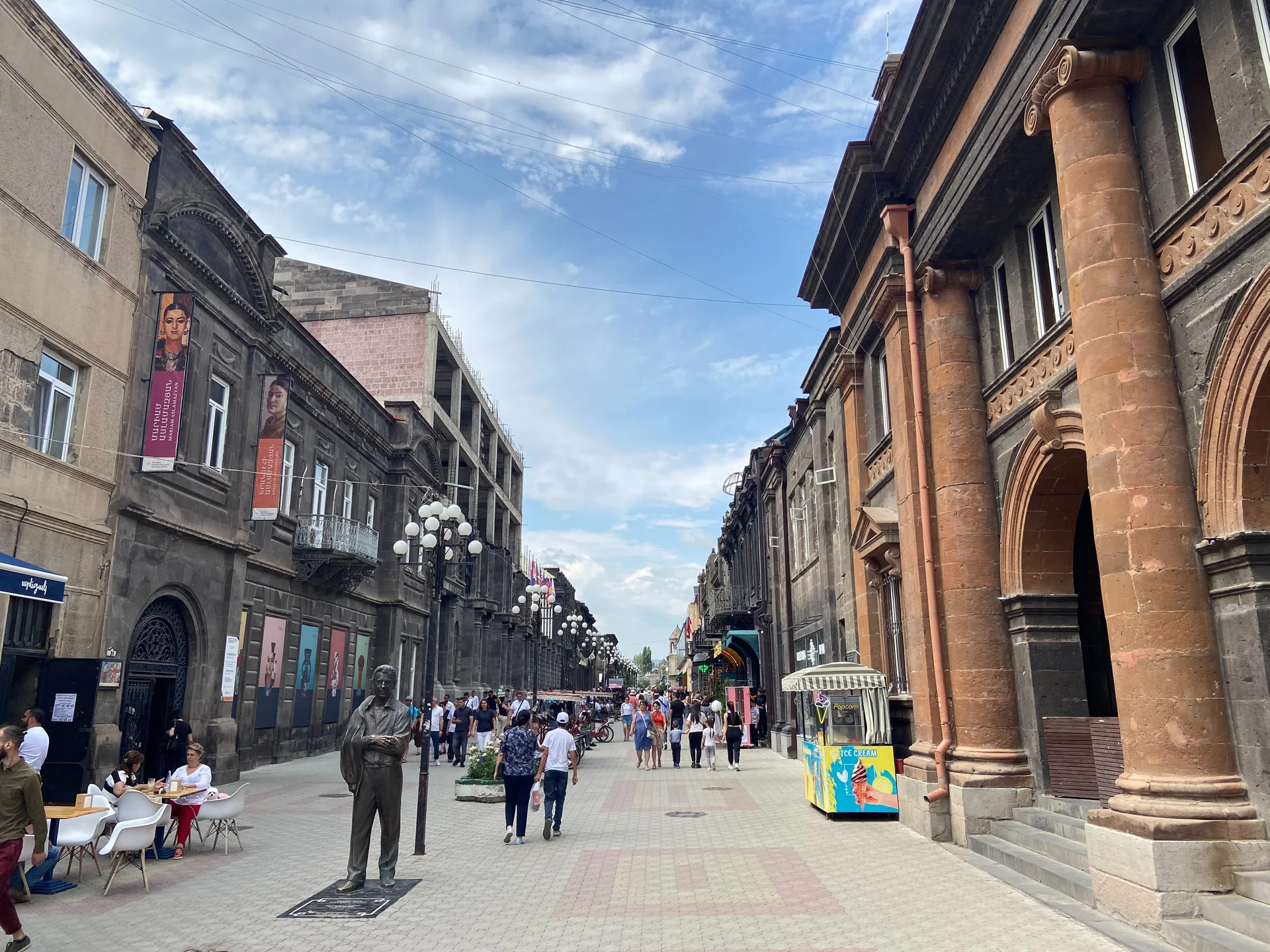 Pedestrians and pavement cafes between carved stone facades on Abovyan Street in Gyumri