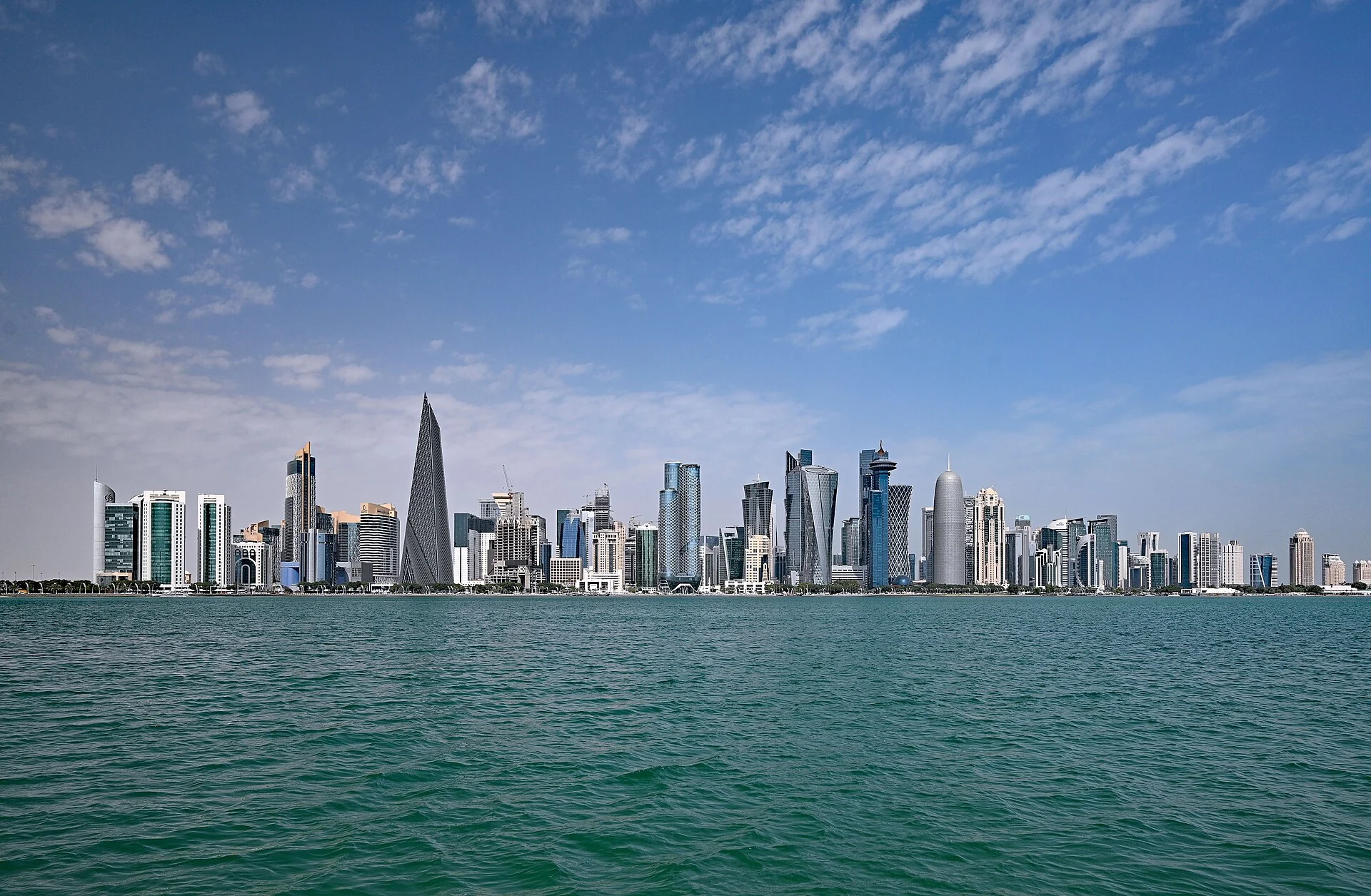 Doha’s West Bay skyline across the water, with its distinctive towers beneath a cloud-streaked sky