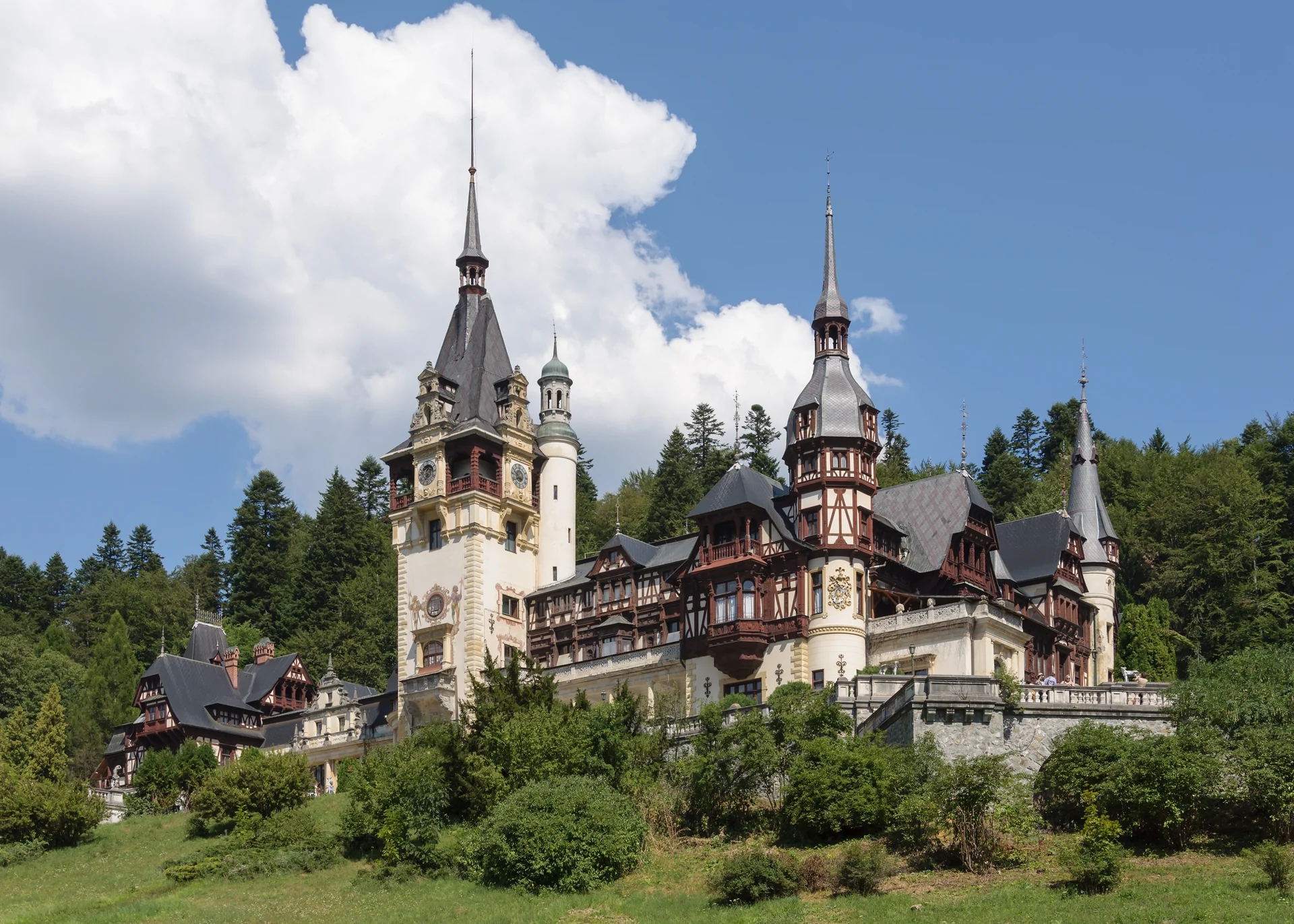 Peleș Castle in Sinaia, Romania, with its ornate towers against the Carpathian forest and blue sky