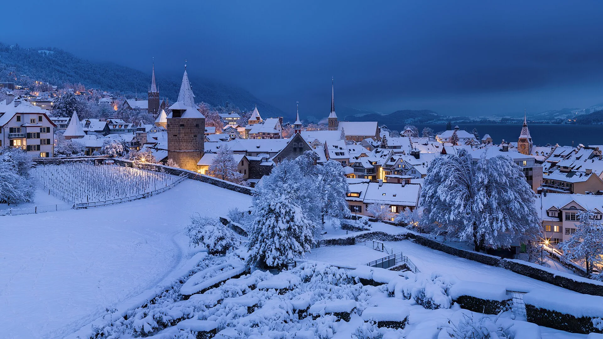 Zug’s snow-covered old town and lake seen from Guggi at dusk.