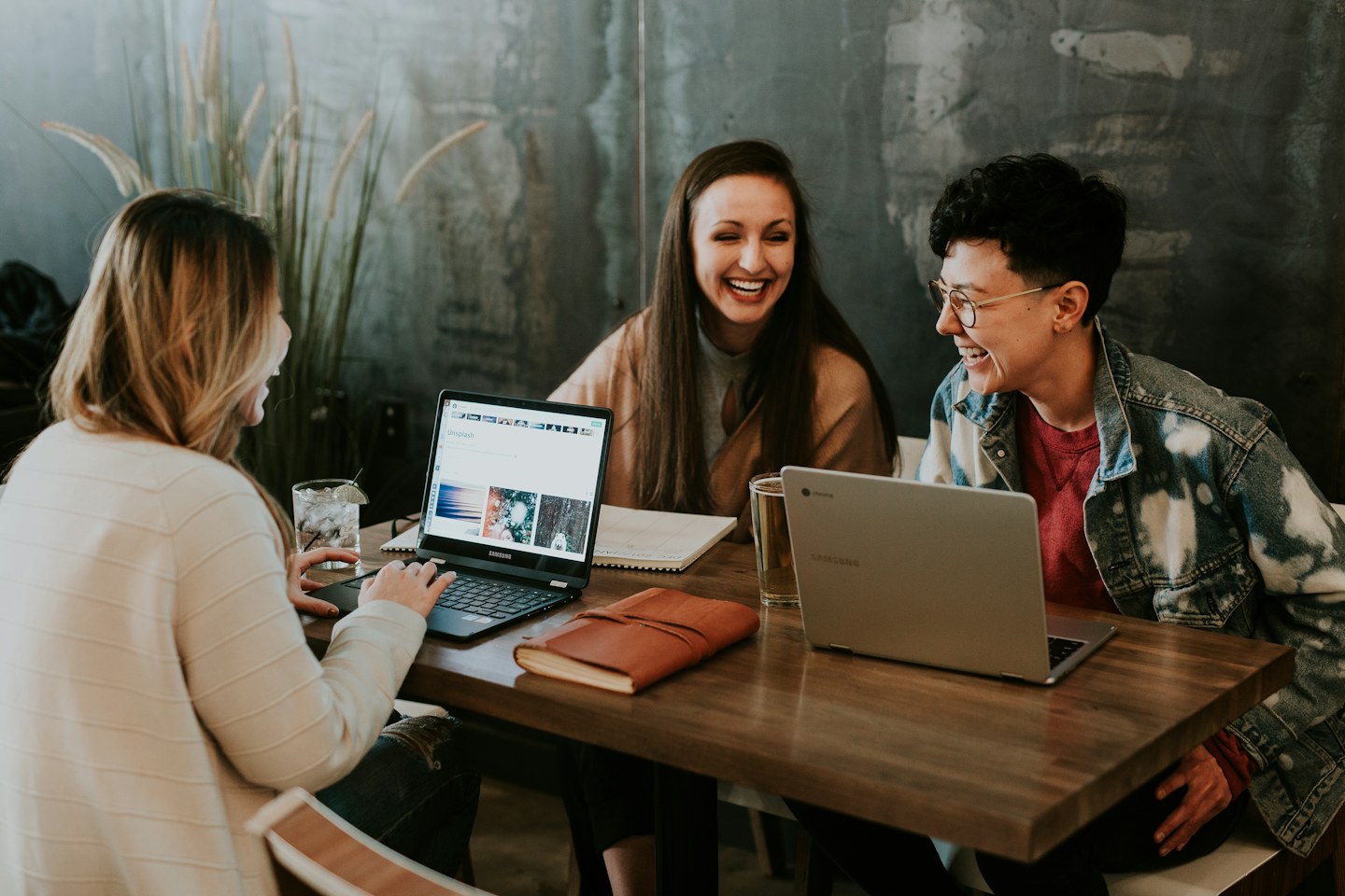 Three people smiling around a table with laptops